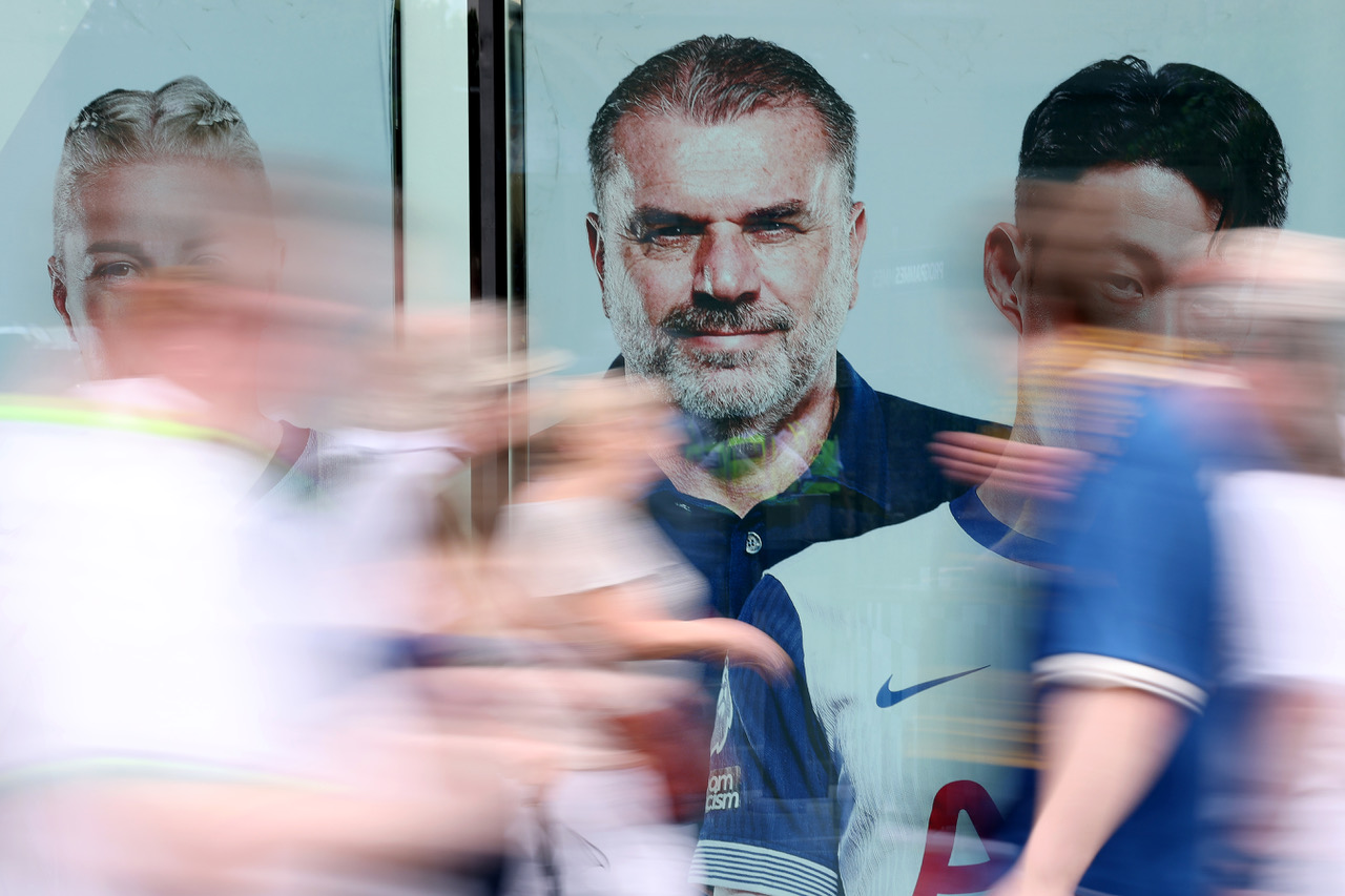 Fans of Tottenham Hotspur walk past a giant picture of Ange Postecoglou,