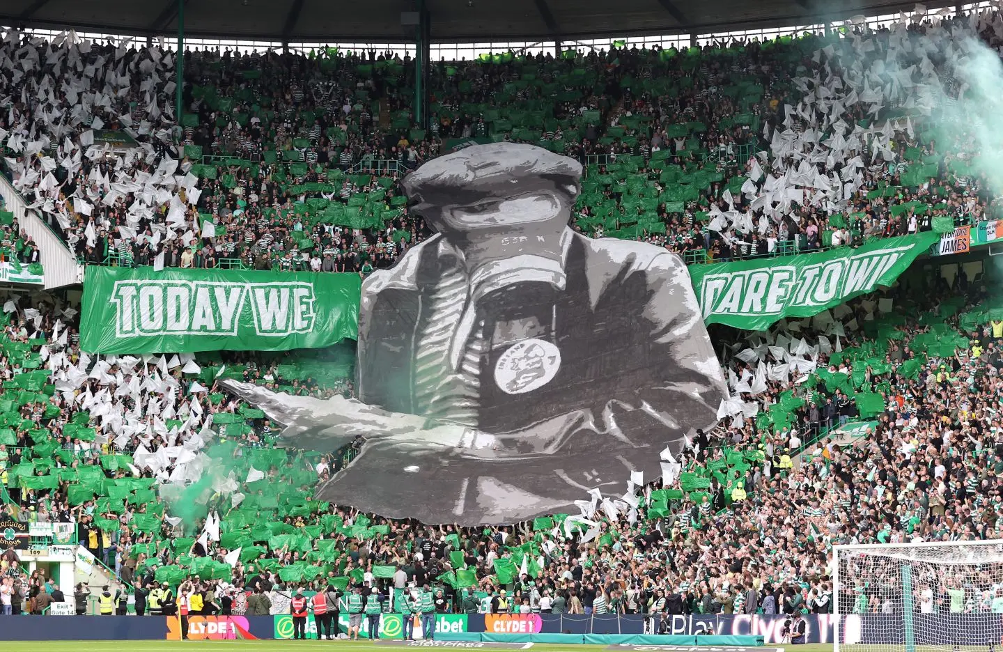 Celtic FC fans display a large tifo with the text 'TODAY WE' and a mural in the stadium.