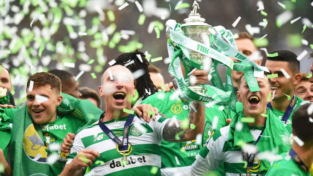 Celtic FC players celebrate with the Scottish Cup trophy amidst confetti.