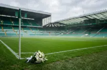 Empty Celtic Park stadium with memorial flowers on pristine green pitch under soft daylight