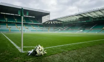 Empty Celtic Park stadium with memorial flowers on pristine green pitch under soft daylight