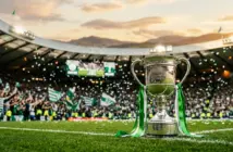 Celtic FC championship trophy with green and white ribbons in packed stadium at sunset