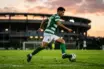 Young midfielder in green and white jersey controlling football during golden hour training session