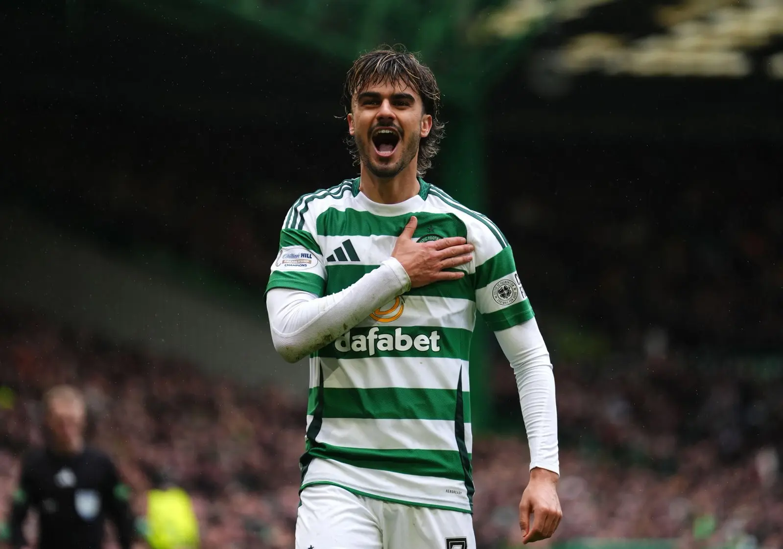 Celtic player celebrates with hand on heart, wearing green and white striped jersey.