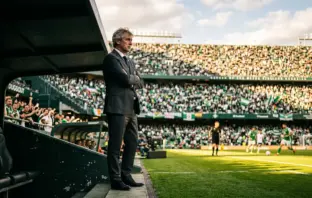 Football manager standing in dugout at Hampden stadium with Celtic supporters in background
