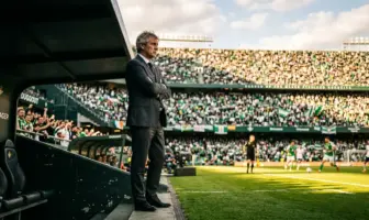 Football manager standing in dugout at Hampden stadium with Celtic supporters in background
