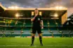 Football referee in black uniform with headset standing authoritatively on stadium pitch under dramatic lighting