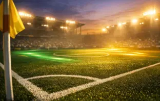 Floodlit football pitch at dusk with emerald and gold lighting, cinematic shadows, corner-flag perspective.