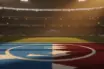 Floodlit stadium pitch with blue-white geometric patterns, crowd silhouettes in stands, dramatic lighting and shadows at golden hour.