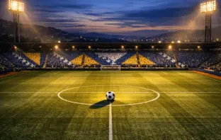 Floodlit stadium at dusk with centre spot football, blue and white flag-coloured stand sections, dramatic shadows.