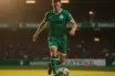 Celtic midfielder in green kit dribbling football on pitch under stadium lights