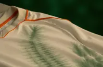 Off-white football kit with green tie-dye hoops and orange trim detail in soft natural lighting