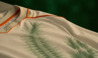 Off-white football kit with green tie-dye hoops and orange trim detail in soft natural lighting