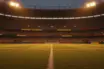 Empty floodlit stadium pitch at dusk with packed stands, golden and blue lighting, no players.
