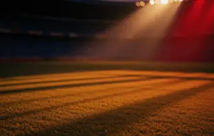 Floodlit stadium at golden hour with dramatic shadows, silhouetted stands, and atmospheric lighting before match.