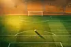 Floodlit stadium pitch at sunset with Côte d'Ivoire orange-green colour scheme, match ball on penalty spot.