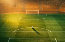 Floodlit stadium pitch at sunset with Côte d'Ivoire orange-green colour scheme, match ball on penalty spot.