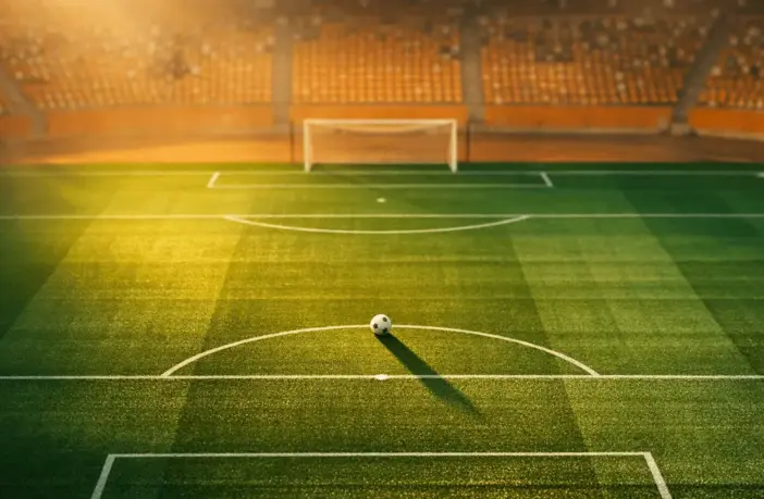 Floodlit stadium pitch at sunset with Côte d'Ivoire orange-green colour scheme, match ball on penalty spot.