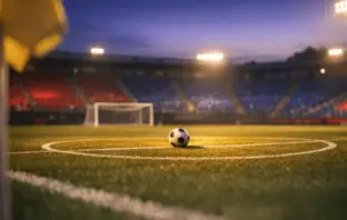 Empty floodlit stadium pitch with centre circle ball, blue and red atmospheric lighting, dusk lighting.