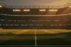 Floodlit football stadium at dusk with packed stands and dramatic pitch lighting, cinematic match atmosphere.