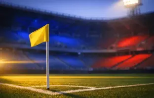 Empty stadium corner with blue-and-red flag-coloured floodlighting, corner flag sharp in foreground, golden dusk light across tiered seating.