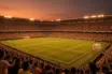 Floodlit World Cup 2026 stadium at golden hour with packed stands in national colours, dramatic pitch shadows, no people on field.