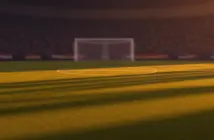 Floodlit football stadium pitch at dusk with packed stands and dramatic shadow patterns, no players visible.