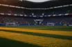 Empty floodlit stadium pitch at dusk with packed stands, dramatic shadows, and golden-hour lighting during international football match.