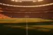 Floodlit international football stadium at sunset with packed stands and shadow patterns across the pitch. No players visible.