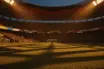 Floodlit stadium with packed stands at golden hour, dramatic shadows, empty pitch, cinematic sports photography.