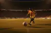 Low-angle stadium shot of boot striking football during evening floodlit match, golden and blue lighting tones.