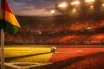 Empty floodlit stadium pitch corner view at dusk, gold and burgundy lighting, match ball on centre spot, sharp shadows.