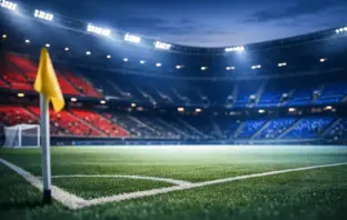 Empty floodlit stadium corner with crimson and blue accent lighting reflecting Haiti's national colours on tiered seating.