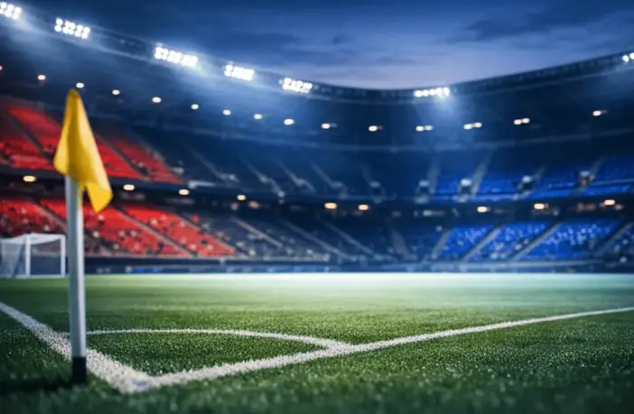 Empty floodlit stadium corner with crimson and blue accent lighting reflecting Haiti's national colours on tiered seating.