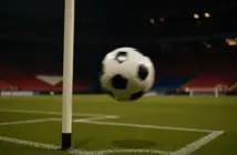 Stadium corner with match ball in motion under floodlights, colour-graded red, blue, white and black.