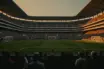 Floodlit stadium pitch at golden-hour with packed stands, dramatic shadows, and architectural geometry in cinematic sports photography.