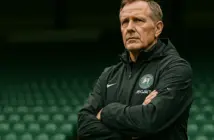 Celtic manager standing in stadium with determined expression, ready for new season challenge