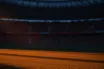Empty floodlit stadium at dusk with dramatic shadow patterns, atmospheric crowd silhouettes in stands, cinematic sports photography lighting.