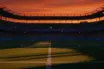 Empty floodlit stadium pitch with dramatic shadows, Dutch orange and Swedish blue atmospheric lighting at dusk.