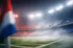 Floodlit stadium corner with red and white atmospheric lighting, empty seats, shallow depth of field.
