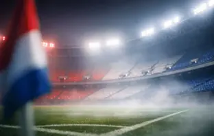 Floodlit stadium corner with red and white atmospheric lighting, empty seats, shallow depth of field.