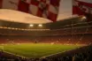Floodlit football stadium at dusk with packed stands and dramatic golden-hour lighting, no players visible.