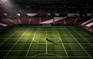 Aerial view of floodlit football stadium with maroon-and-white colour scheme, ball on centre spot, empty stands with bunting