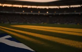 Empty floodlit stadium pitch with blue and yellow shadow patterns and packed stands at dusk