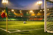 Floodlit stadium corner view with green and gold accent lighting, empty pitch, goal net, cinematic sports photography.