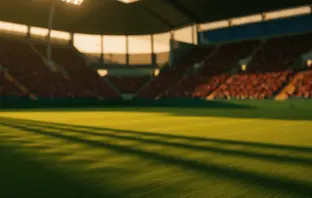 Floodlit stadium at dusk with green and yellow lighting, packed stands, dramatic shadows on pitch.