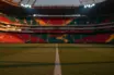 Modern floodlit football stadium at dusk with geometric pitch markings, red and green crowd sections, dramatic shadows.