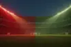 Floodlit stadium at golden hour with packed stands, dramatic shadows, Swiss red and Algerian green lighting palette.