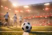 Floodlit football pitch corner with red and white accent lighting, motion-blurred players, and ball in sharp focus on centre circle.