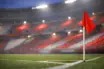 Empty stadium corner with red and white atmospheric lighting, floodlit pitch markings in soft focus, evening mood.